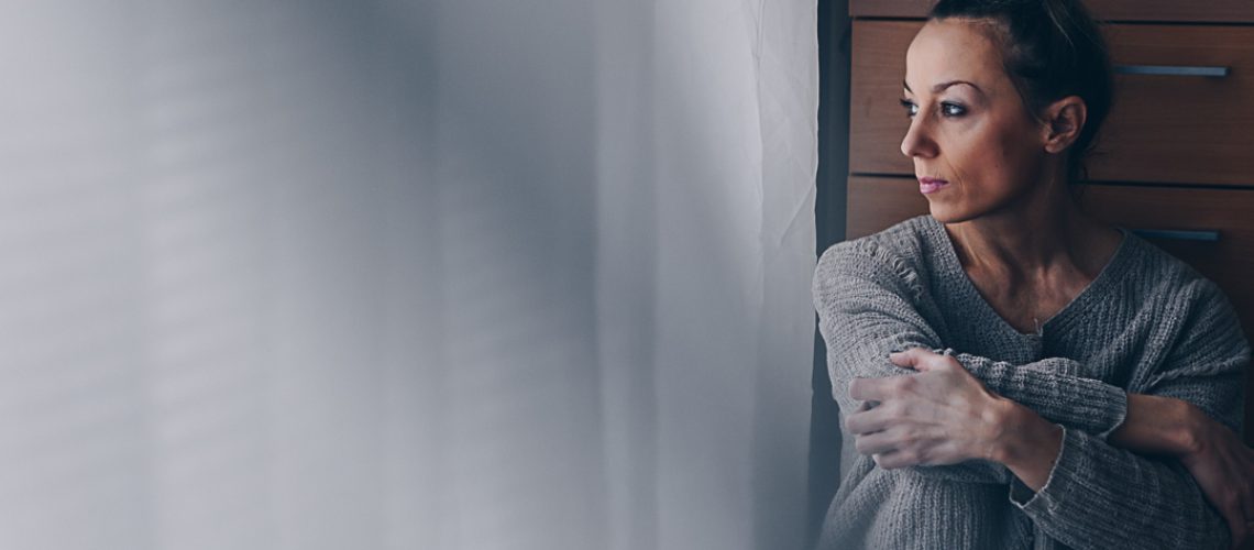 Beautiful sad woman sitting on the floor looking at the window. Depression and despondency.