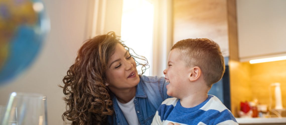 Kind mother helping her son doing homework in kitchen. Mother Helping Son With Homework At Table. Children's creativity. Portrait of smiling mother helping son with homework in kitchen at home